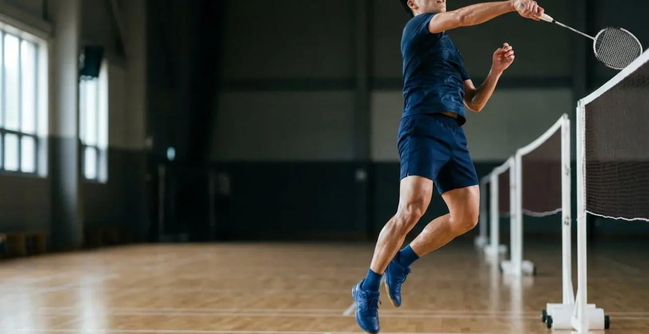 Athlète de badminton en plein saut explosif démontrant la puissance musculaire des jambes au-dessus du filet