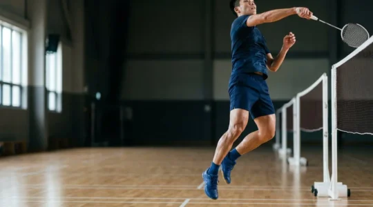 Athlète de badminton en plein saut explosif démontrant la puissance musculaire des jambes au-dessus du filet