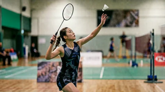 Joueur de badminton en pleine exécution d'un fast drop depuis le fond de court, transformant une position défensive en attaque